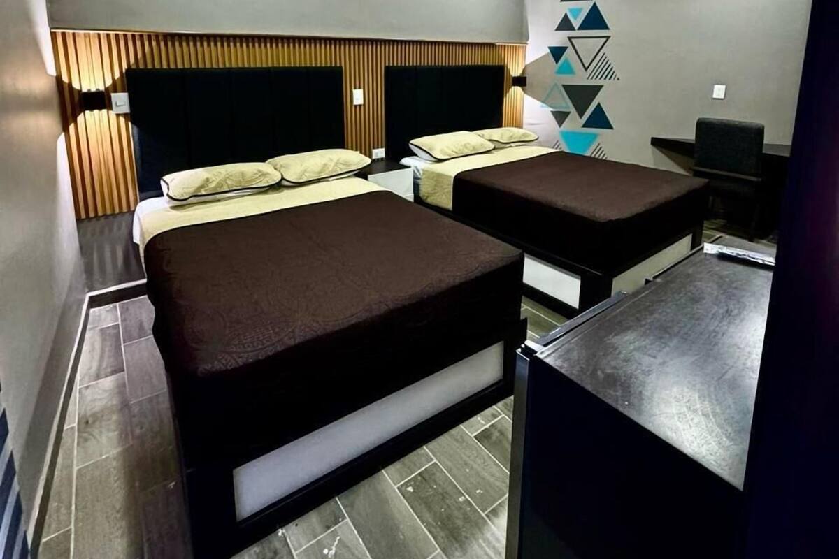 Een moderne hotelkamer met twee bedden, een bureau en een aan de muur bevestigde televisie.