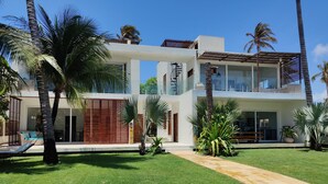 Una casa moderna de dos pisos con césped cuidado, palmeras y un cielo azul despejado.