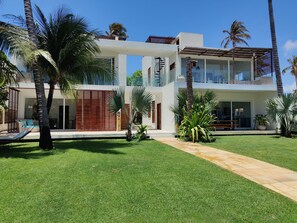 A modern two-story house with a well-maintained lawn, palm trees, and a clear blue sky.