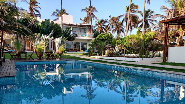 Una piscina rodeada de palmeras y un edificio blanco con un balcón.