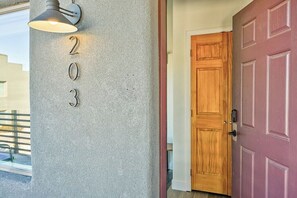 Une entrée d’immeuble avec le numéro « 203 » sur un mur texturé, une porte en bois et un luminaire.