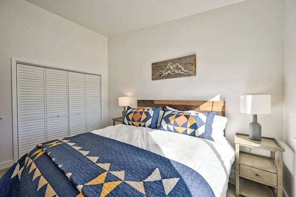 A bedroom with a bed, a nightstand, a lamp, a wall-mounted artwork, and a closet.