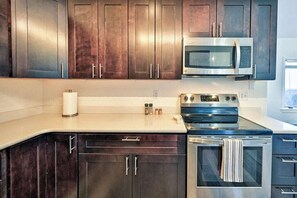 Une cuisine avec des meubles de couleur bois foncé, un four à micro-ondes en acier inoxydable, un four classique et un plan de travail sur lequel on trouve un rouleau d’essuie-tout et quelques récipients à épices.