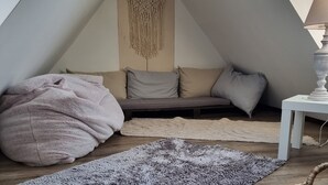 A cozy loft bedroom with a sloped ceiling, a gray sofa, a large gray rug, and a macrame wall hanging.