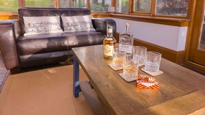 Una habitación con sofá de cuero, una mesa de centro de madera, una botella de licor y varios vasos.