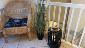A wicker chair with a floral pillow, a tall potted plant, and a black lantern beside a white railing. - Ferienhof Eckhoff apartment no. 4 with south-facing terrace (Fehmarn)