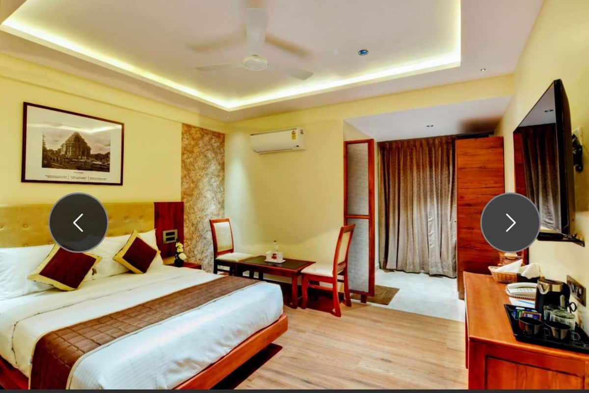 A hotel room with a bed, a desk, a chair, a TV, and an air conditioning unit.