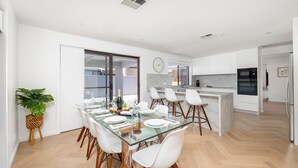 Una cocina moderna con armarios blancos, una isla central y un comedor con mesa de vidrio y sillas blancas.