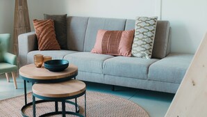 A modern living room with a grey sofa, two round wooden tables, and a patterned rug. - Big lodge | 6 persons (Voorthuizen)