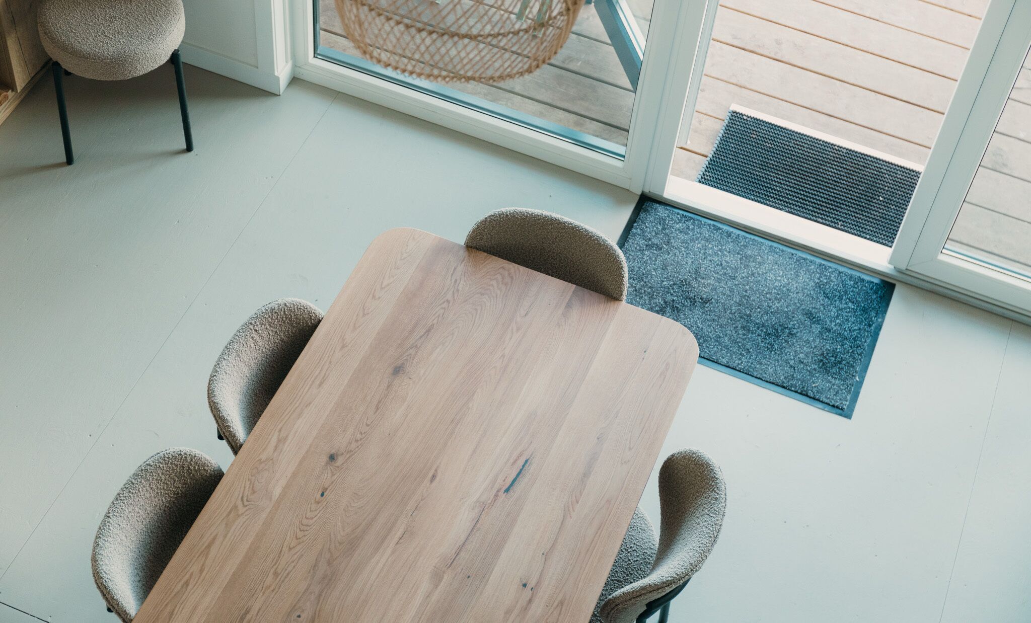 Een houten tafel met vier stoelen, een rieten fauteuil en een glazen deur naar buiten.
