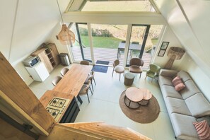 A modern interior with a dining area, kitchen, and seating space, featuring a large window and a staircase. - Big lodge | 6 persons (Voorthuizen)