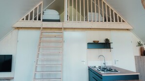 A loft bedroom with a wooden staircase, a small kitchenette, and a balcony with a railing. - Big lodge | 6 persons (Voorthuizen)