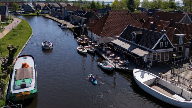 A canal lined with traditional buildings, boats docked along the water, and a small boat in the middle. - Safari tent Heeg 4 persons (Heeg)