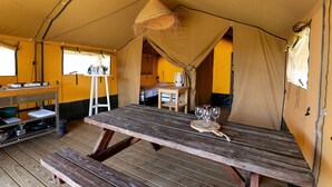 A tented accommodation with a wooden picnic table, a small dining table, and a hanging light fixture. - Safari tent Heeg 4 persons (Heeg)