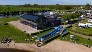 A marina with boats, a building with a solar panel, and a sandy area with people. - Safari tent Heeg 4 persons (Heeg)