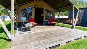 A tented outdoor area with two red chairs and a table, surrounded by wooden deck and grassy area. - Safari tent Heeg 4 persons (Heeg)
