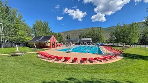 A swimming pool with red lounge chairs and a small pavilion in a park. - 4 bedroom Eagle Vail townhome on golf course; minutes to Vail and Beaver Creek (Avon)
