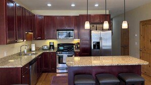 A kitchen with dark wood cabinets, stainless steel appliances, granite countertops, and pendant lighting. - 4 bedroom Eagle Vail townhome on golf course; minutes to Vail and Beaver Creek (Avon)