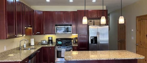 A kitchen with dark wood cabinets, stainless steel appliances, granite countertops, and pendant lighting.