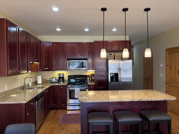 A kitchen with dark wood cabinets, stainless steel appliances, granite countertops, and pendant lighting.