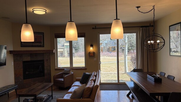 A living room with a fireplace, a sofa, a dining table, and pendant lights. - 4 bedroom Eagle Vail townhome on golf course; minutes to Vail and Beaver Creek (Avon)