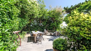 An outdoor patio with a wooden table and chairs, surrounded by lush greenery and trees. - Samzun, close to the beach, garden & sea view (Bangor)