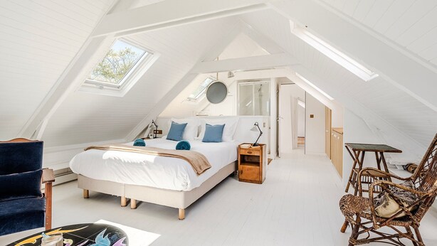 A spacious attic bedroom with a large bed, a chair, and a small table. - Samzun, close to the beach, garden & sea view (Bangor)