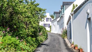 A narrow street flanked by white buildings with blue shutters, lush greenery, and a clear sky. - Samzun, close to the beach, garden & sea view (Bangor)