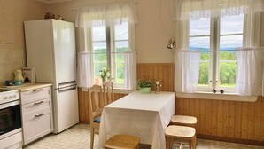 A kitchen with a refrigerator, stove, and wooden chairs around a table.