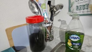 A kitchen counter with a sink, a jar with a red lid, a bottle of Dawn dish soap, and a decorative plate with a floral design.