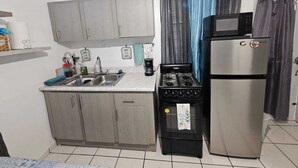 A compact kitchen with grey cabinets, a sink, a stove, and a refrigerator.