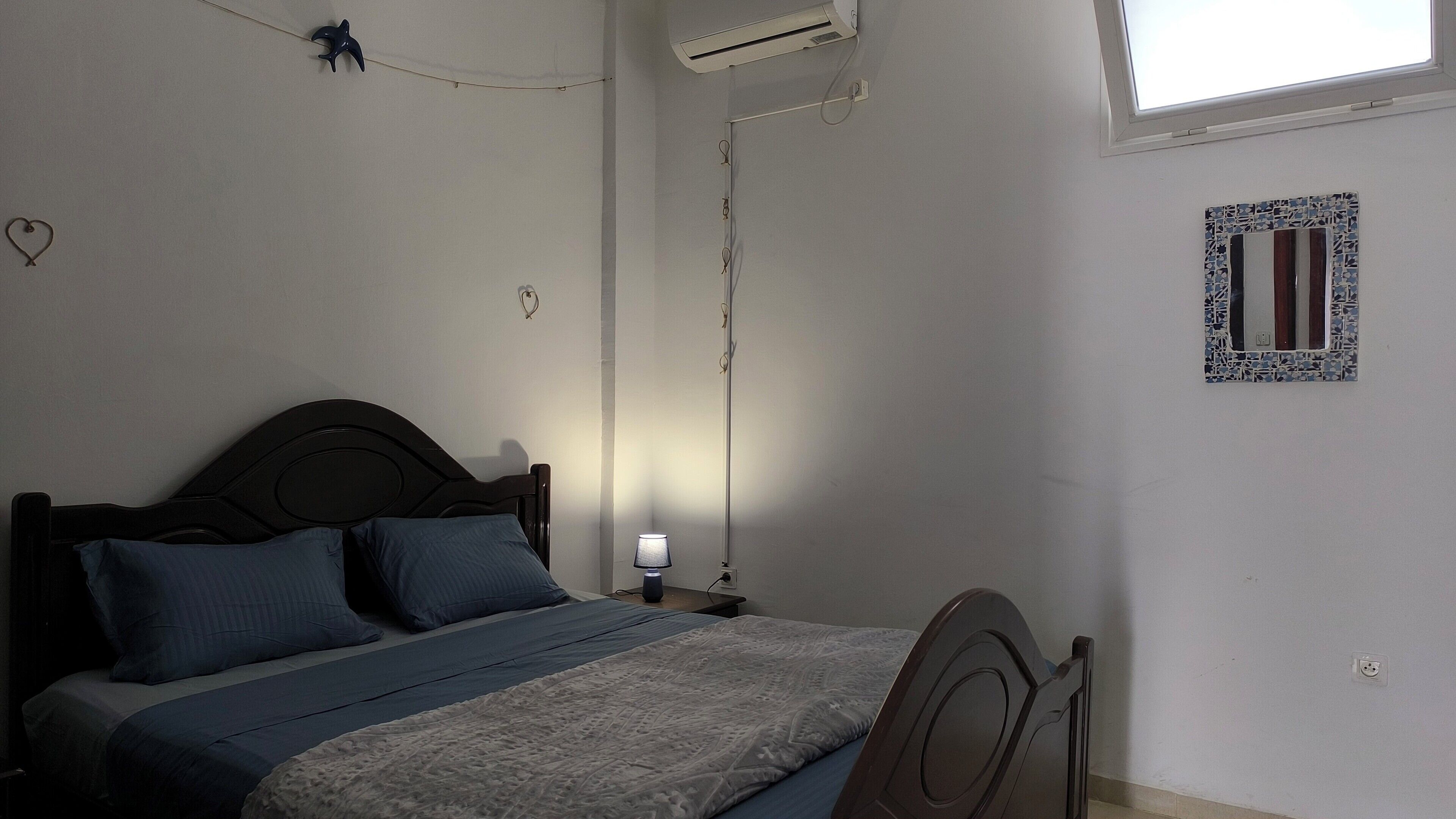 Un dormitorio con cama, lámpara de noche y ventana.