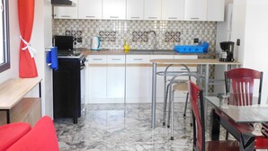 Una cocina compacta con armarios blancos, salpicadero de azulejos, cafetera y comedor con mesa y sillas.