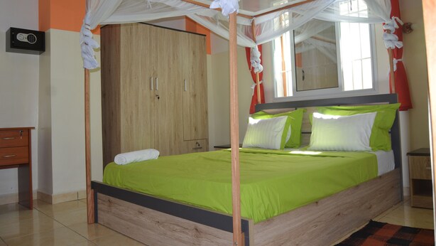 Una cama con estructura de madera y ropa de cama verde, un armario de madera y una mesita de noche con una lámpara.