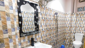 Un baño con lavamanos blanco, ducha e inodoro. Las paredes están cubiertas de azulejos con un diseño decorativo.