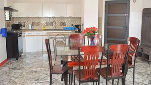 Una cocina con armarios blancos, salpicadero de azulejos, cafetera y una mesa de comedor con sillas.