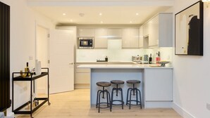 A modern kitchen with white cabinets, a microwave, and a bar area with stools. - The Melbray Gem - 2bdr Apartment With Courtyard (London)