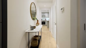 A narrow hallway with a white wall, a large mirror, and a small table with a vase and a bowl. - The Melbray Gem - 2bdr Apartment With Courtyard (London)