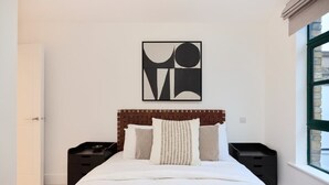 A modern bedroom with a wooden headboard, a large bed with white bedding, and a geometric wall art piece. - The Melbray Escape - Trendy 2bdr Apartment (London)