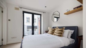 A bedroom with a bed, a window, a mirror, and a shelf with books. - The Shoreditch Retreat - Inviting 2bdr Apartment (London)