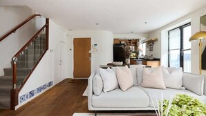 A modern living room with a grey sofa, wooden staircase, and a kitchen in the background. - The Shoreditch Retreat - Inviting 2bdr Apartment (London)