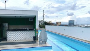 Une piscine sur le toit, avec un espace bar, une vue sur la ville et un ciel dégagé.