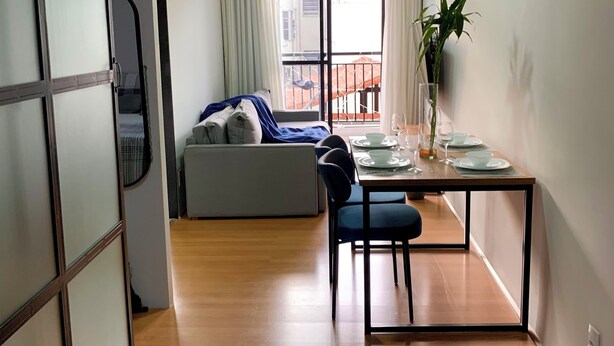 Een moderne woonkamer met een bank, een eettafel gedekt voor twee personen, en een groot raam met gordijnen.