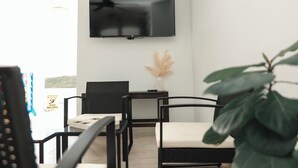 Une chambre moderne avec un téléviseur à écran plat fixé au mur, une petite table surmontée d’un vase contenant des herbes de la pampa séchées, et deux chaises noires.