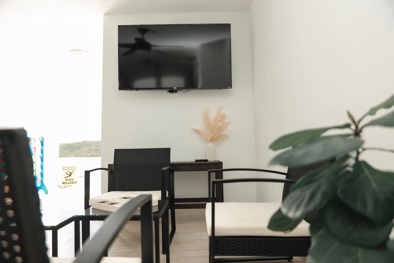 Uma sala de estar moderna com uma televisão de tela plana na parede, uma mesinha com um vaso de plantas secas e duas cadeiras.