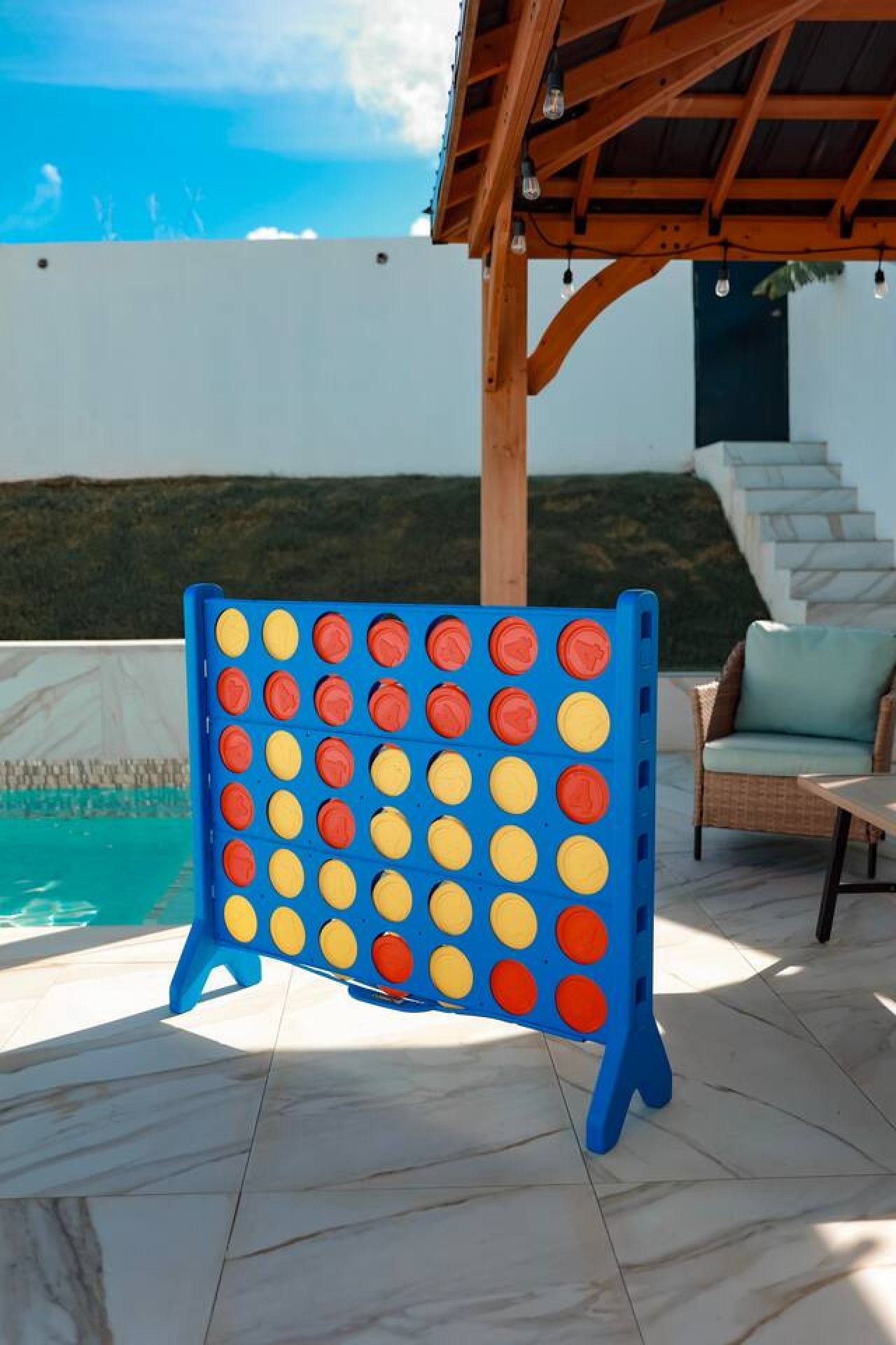 A board game setup outdoors with a pool and a covered seating area.