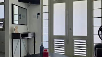 A room with a round table, a flat-screen TV mounted on the wall, and a large window with blinds.