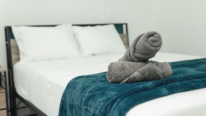 Un lit recouvert d’une couverture turquoise et sur lequel est posée une serviette enroulée.