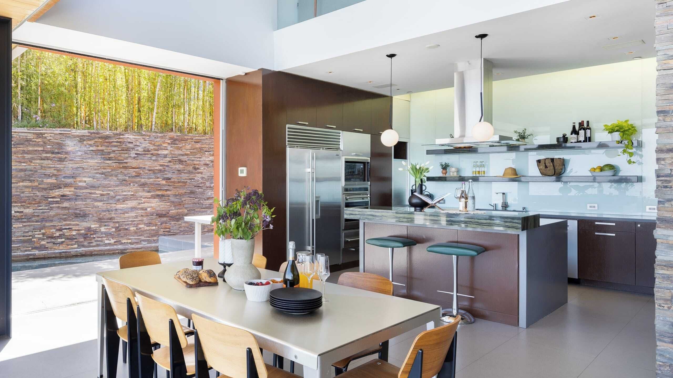 A modern kitchen with a large island, stainless steel appliances, and a dining area with wooden chairs.