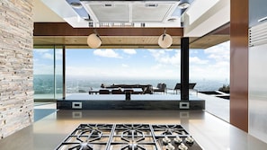 A modern kitchen with a gas stove, large windows, and a dining area with a view of the city. - Hollywood Overlook by Avantstay Private Pool + Hot Tub Panoramic Views (Los Angeles)